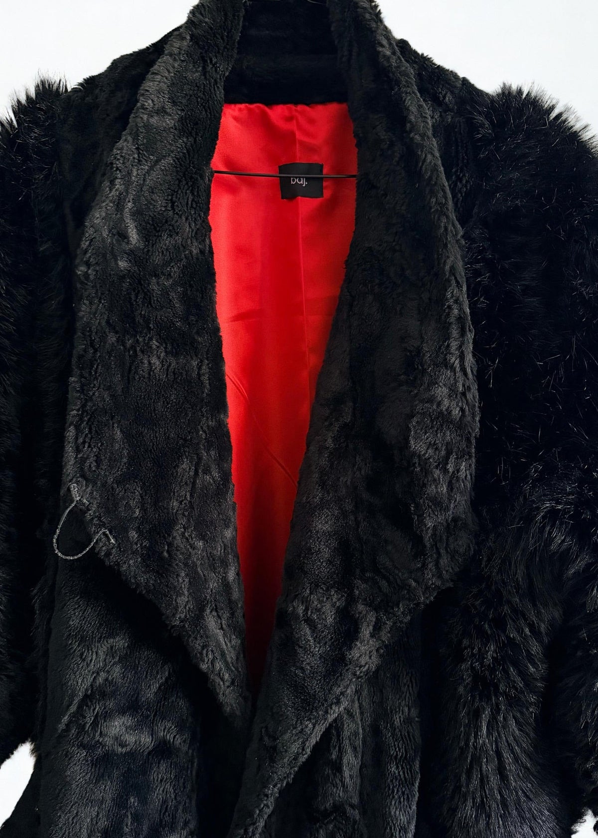 A black faux fur coat with a vibrant red lining, shown hanging on a black hanger against a plain white background.