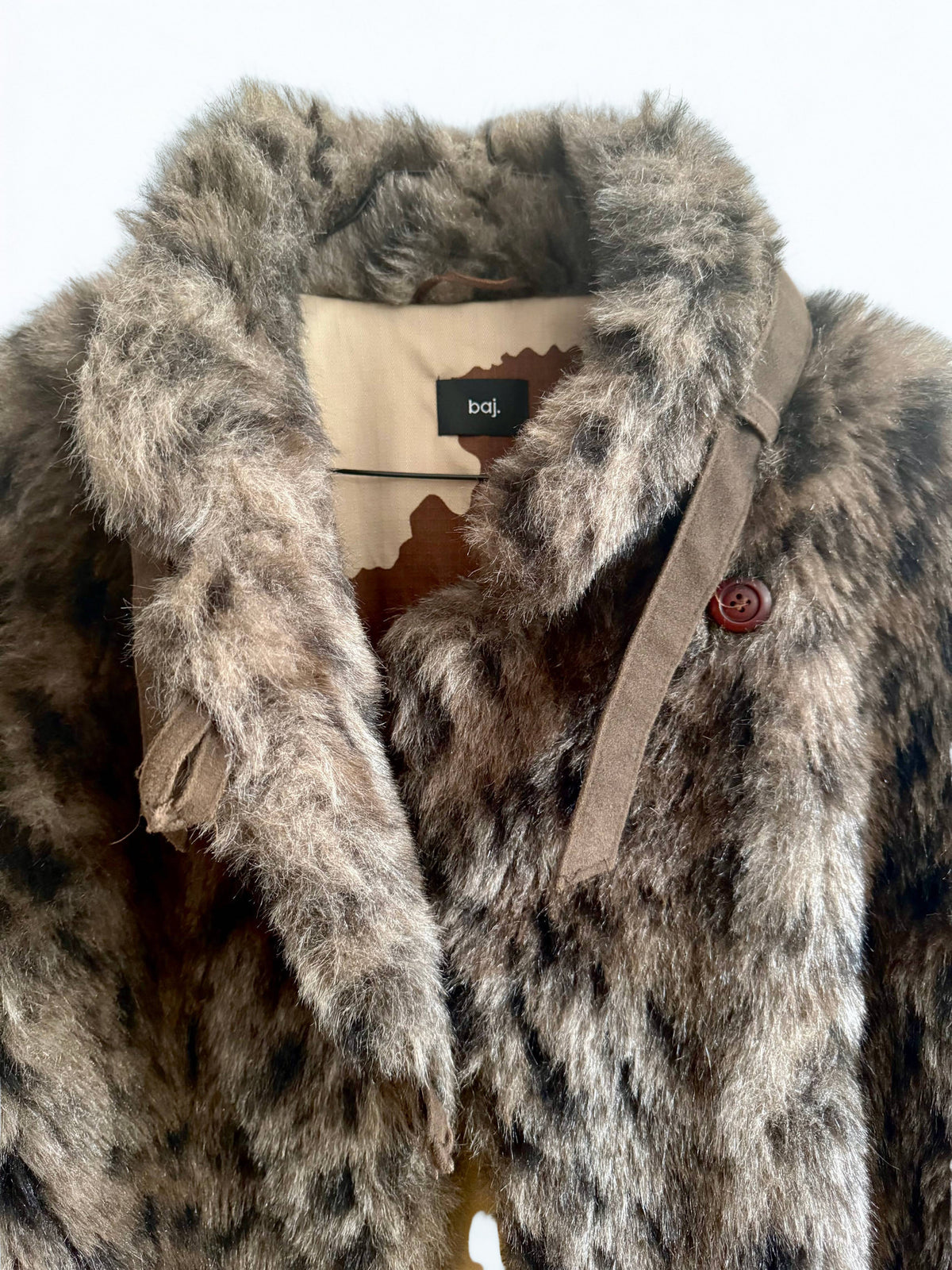 A close-up of a brown and gray faux fur coat with a wide collar, a tan belt, and a small brown button, shown against a plain white background. The brand label reads 'b&j'.