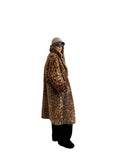 Person wearing a leopard print coat in a room with white walls and wooden flooring.