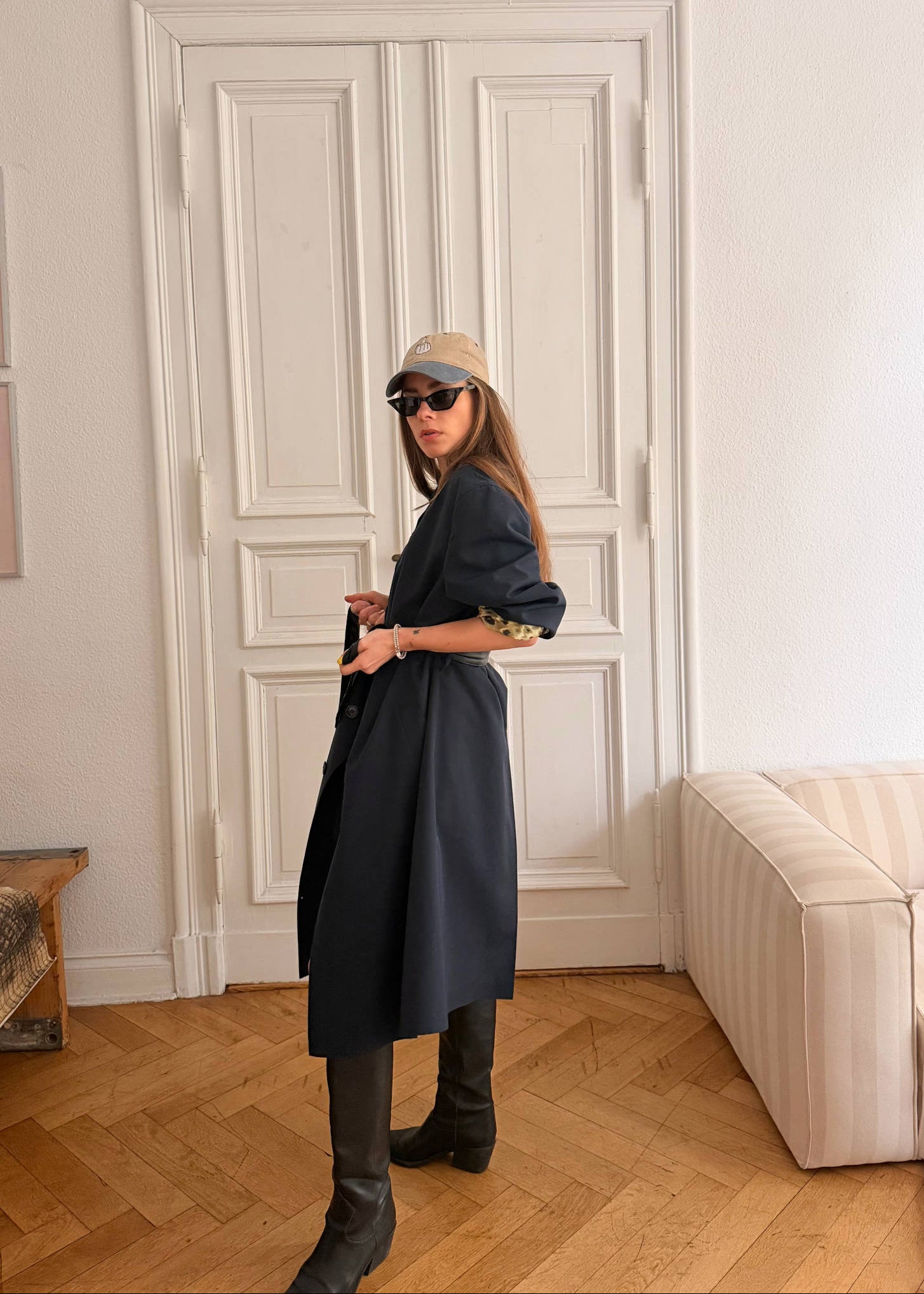 Person wearing a dark coat and hat in a room with a white door and beige sofa.