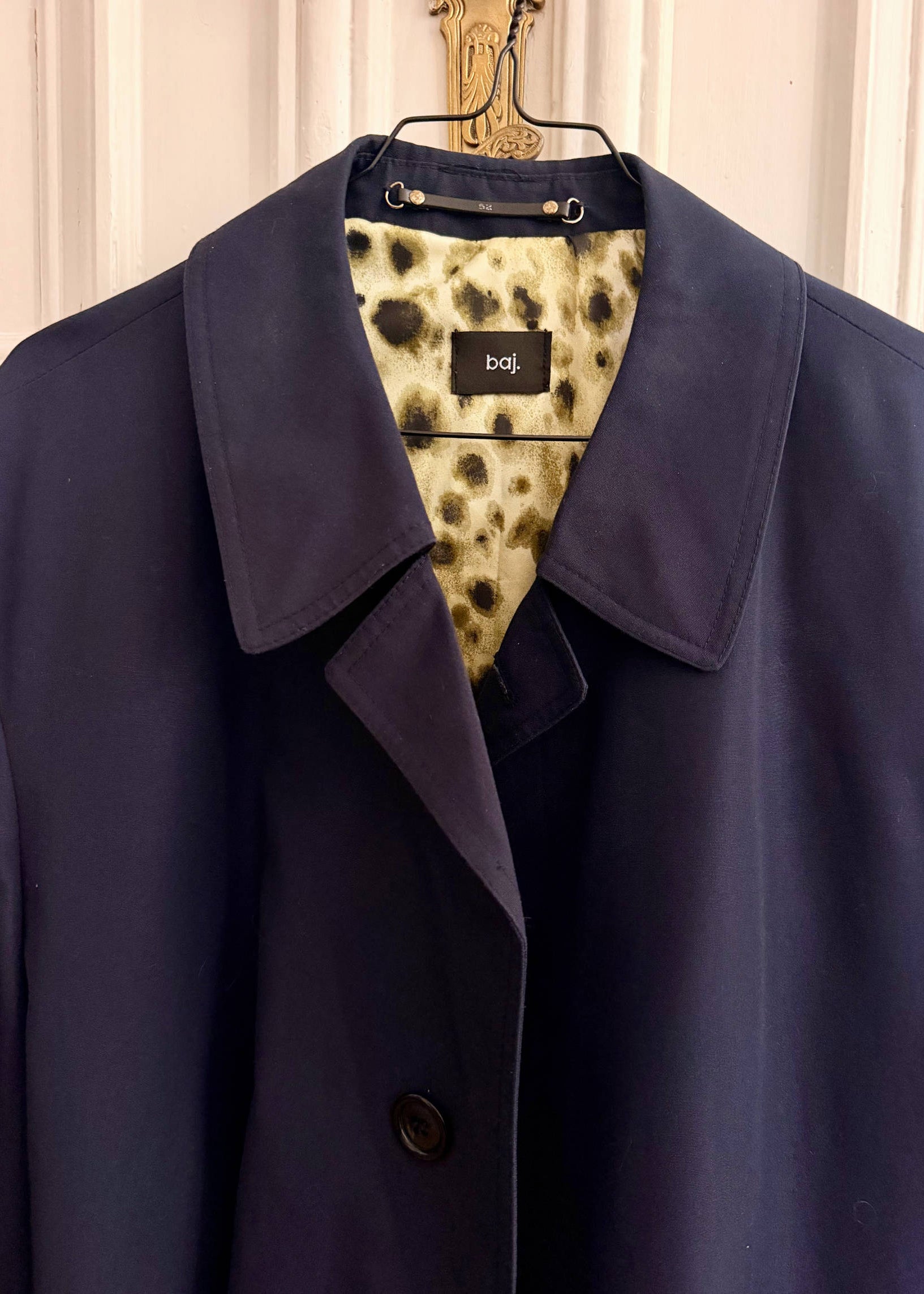 Navy blue coat on a hanger with a patterned tag displaying 'baj'.