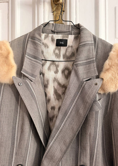 A gray pinstripe blazer jacket with beige faux fur trim on the collar and shoulders, featuring a leopard-print lining and a black 'bdt.' label at the inner collar, hanging on a black hanger against a white paneled door.