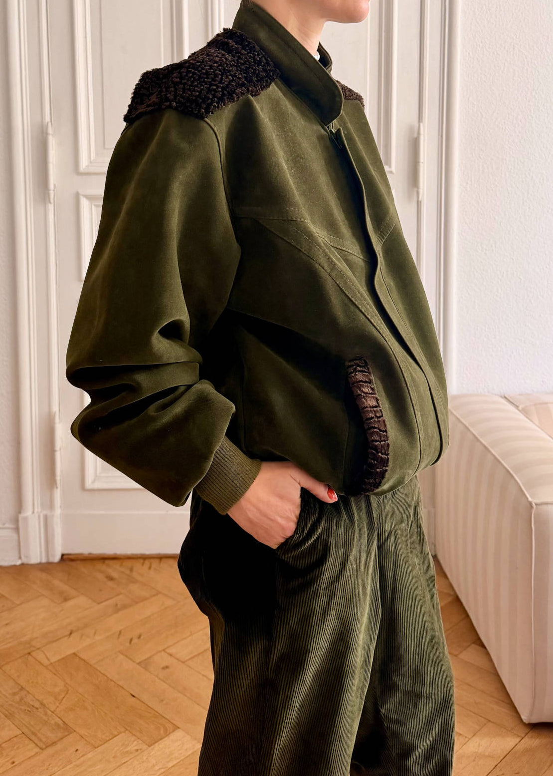 A woman wearing an olive green vegan suede jacket with furry brown lace shoulder detailing