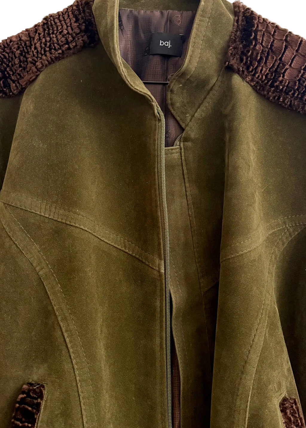 An olive green suede jacket with dark brown textured shoulder yokes and matching pocket trim, hanging on a black hanger against a white background. The brand label 'boj' is visible inside the collar.