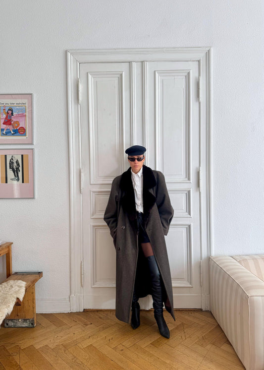 Person wearing a long coat and black boots standing in a room with a white door and wooden floor.