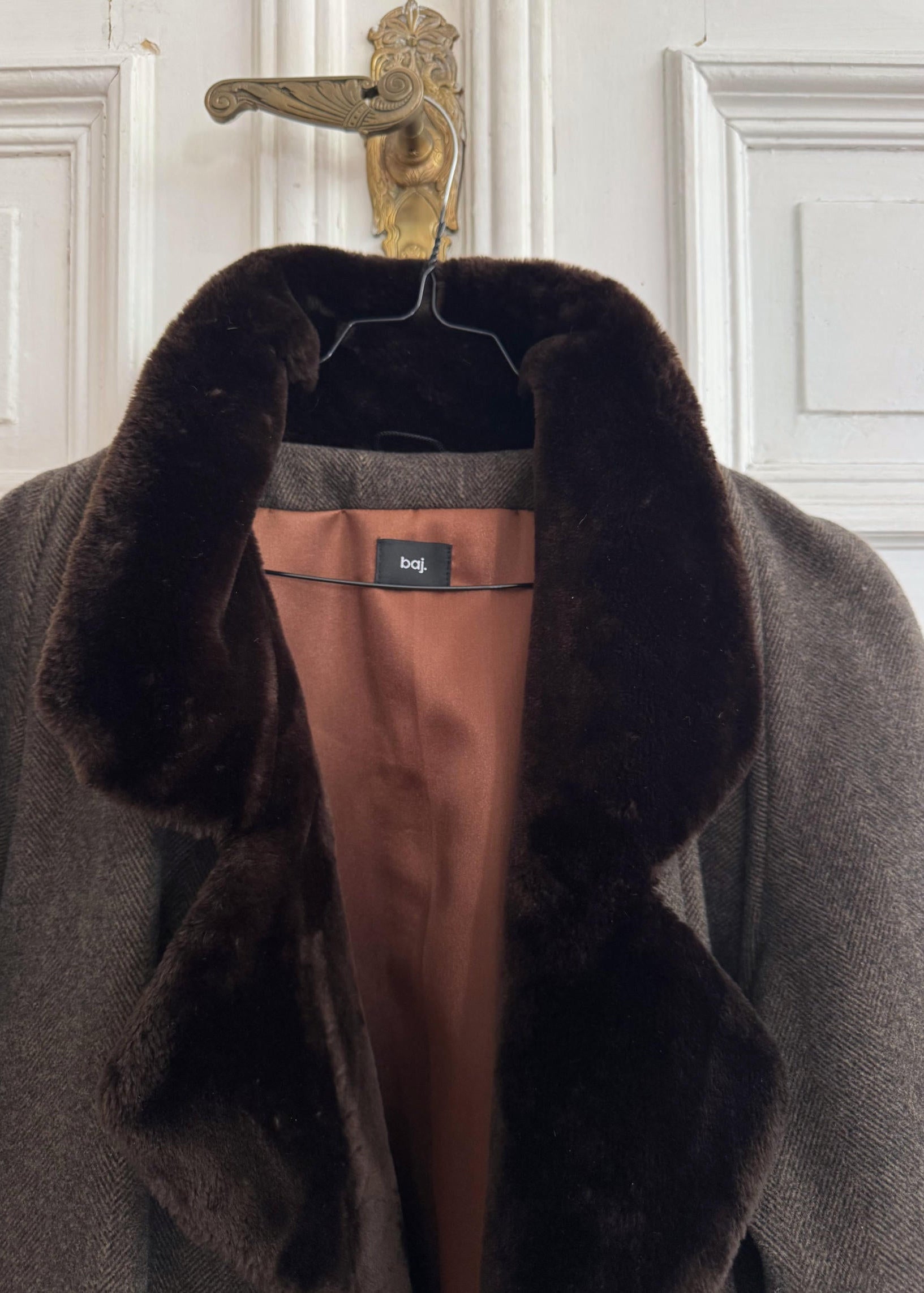 Gray coat with fur collar on a hanger against a white paneled wall.