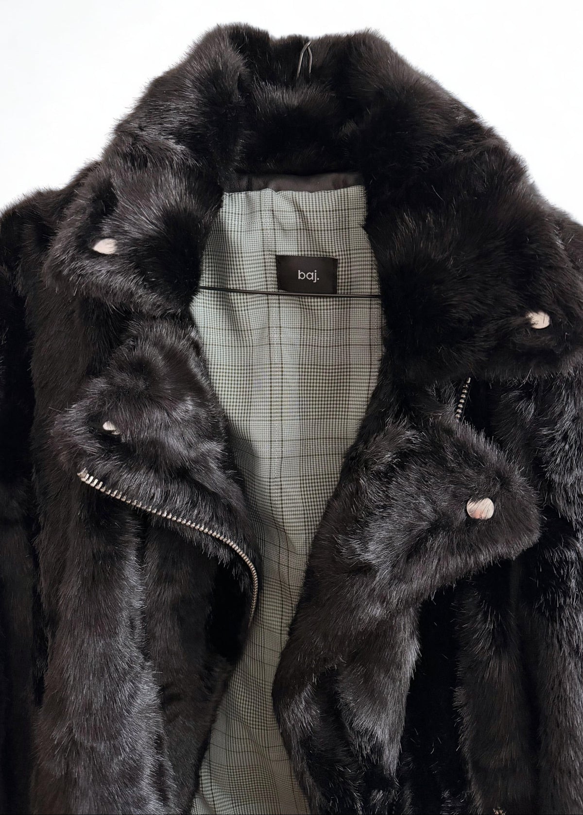 A close-up of a black faux fur jacket with a light gray plaid lining and silver-tone snap buttons, shown against a plain white background.
